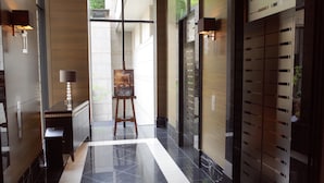 A modern lobby with a polished marble floor, a wooden reception desk, a standing easel with a poster, and a wall-mounted elevator with a glass door. - Hotel Trusty Tokyo Bayside (Tokyo)
