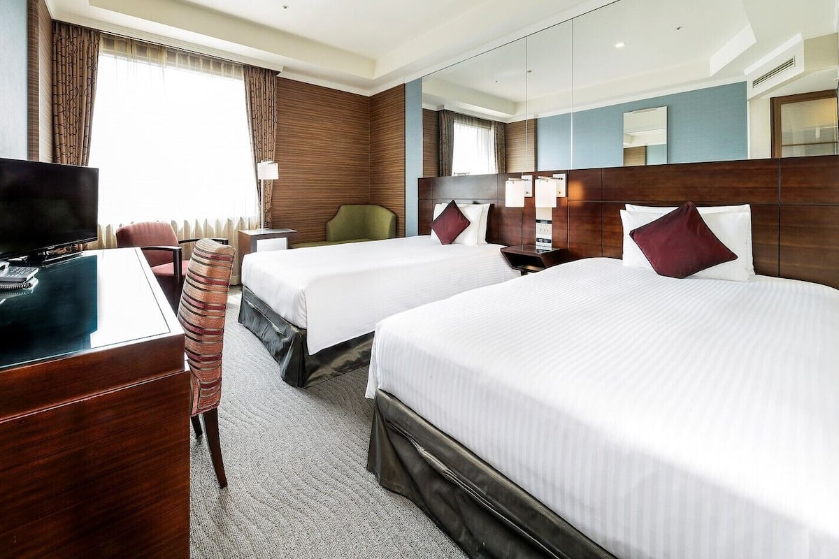 A hotel room with two beds, a desk with a telephone, a chair, and a large mirror.