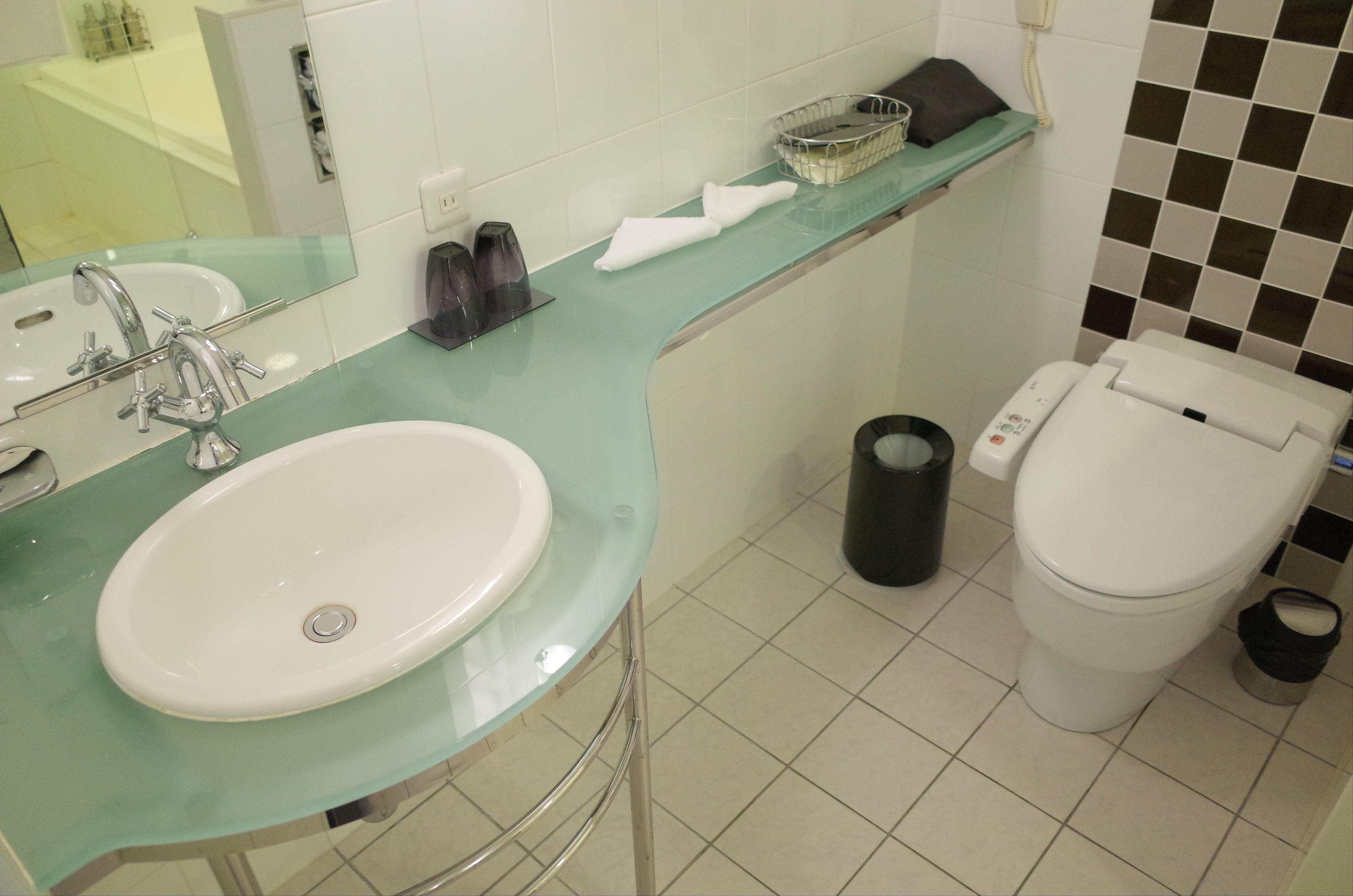 A bathroom with a glass sink, a toilet, and a trash bin.