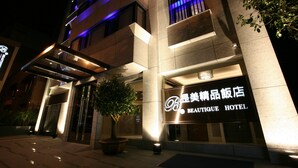 Een hotel met meerdere verdiepingen, een moderne gevel, verlichte signage en een potplant ervoor.