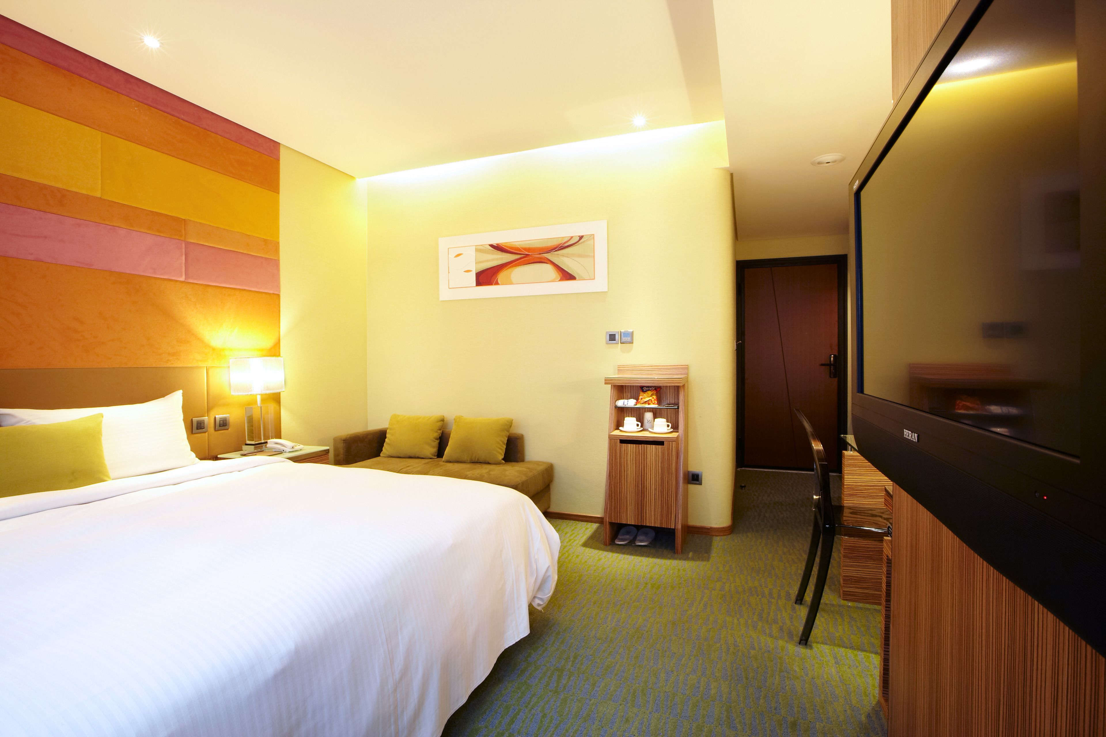 A hotel room with a large bed, a desk with a computer, a television, and a shoe rack.