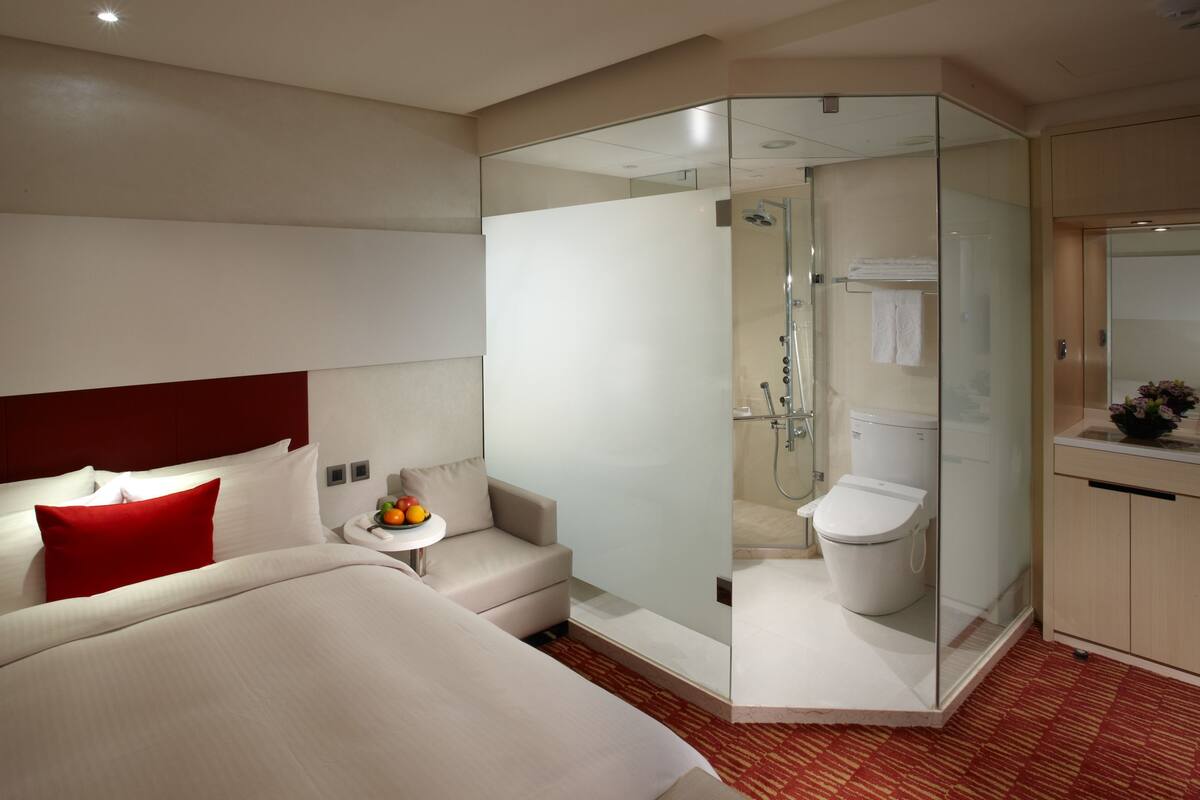 Een moderne hotelkamer met een bed, een zithoekje, een douchecabine van glas en een badkamer met toilet en wastafel.