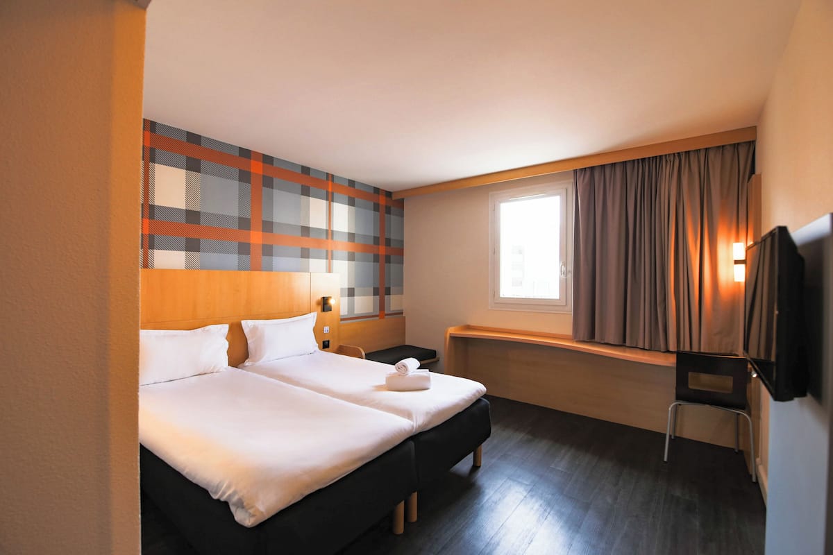 Habitación de hotel con dos camas, un televisor, un ventanal con cortinas y una pared con estampado escocés.