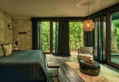 A bedroom with a bed, a chair, a round table, and a large window with curtains.