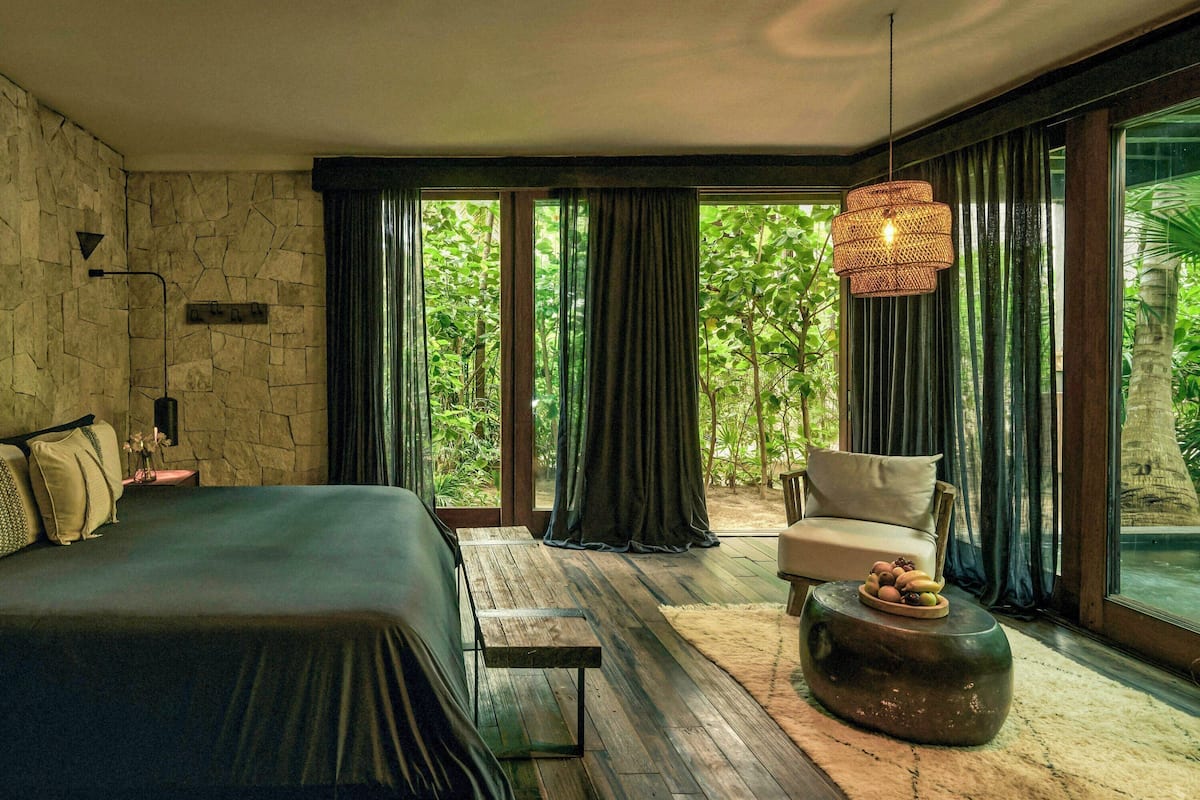 A bedroom with a bed, a chair, a round table, and a large window with curtains.