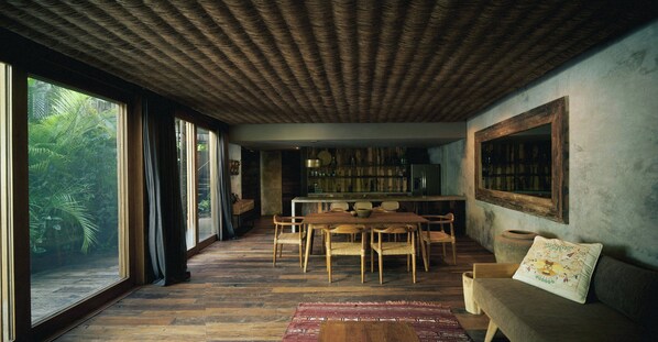 A spacious room with a large dining table, wooden chairs, a sofa, and a bookshelf.