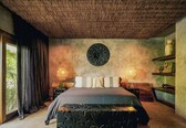 A bedroom with a bed, a woven ceiling, a wall decoration, and a shelf with items.