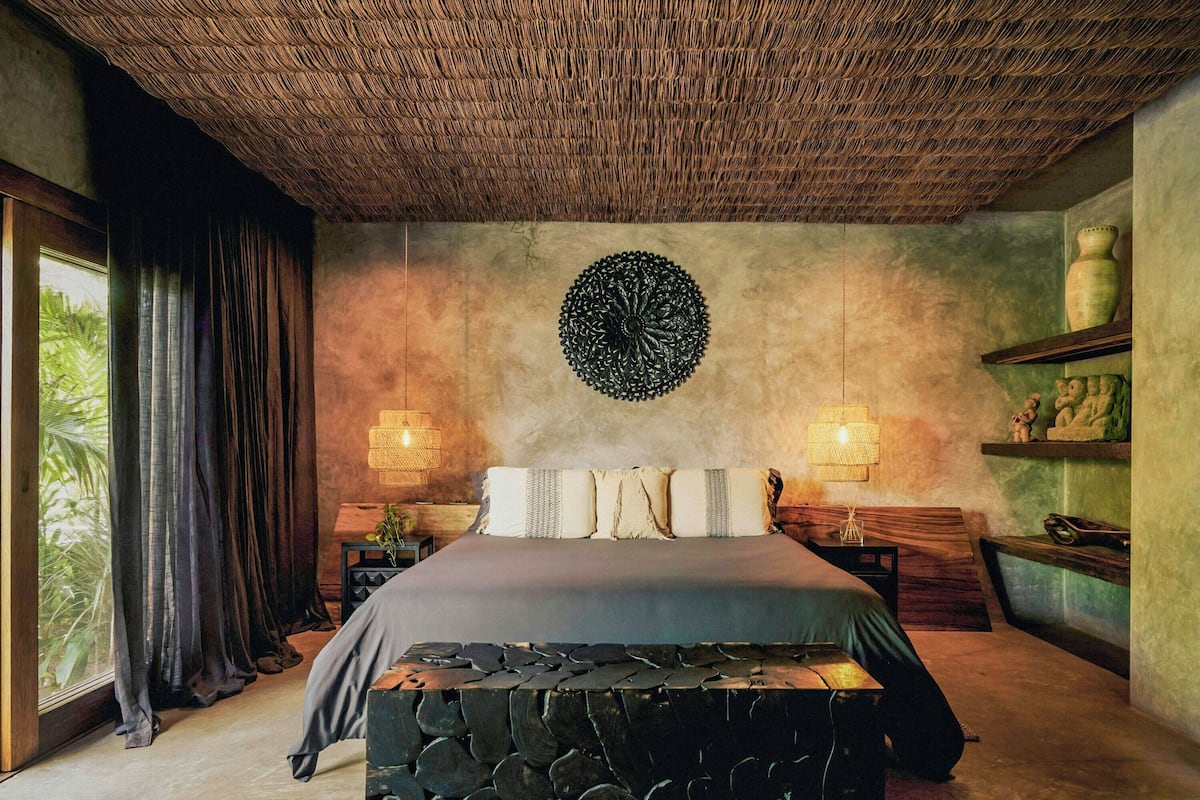 A bedroom with a bed, a woven ceiling, a wall decoration, and a shelf with items.