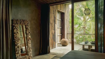 Una habitación con un espejo grande, una cama, una puerta de madera que da a un balcón y vistas al verdor exterior.