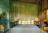 A room with a bed, green curtains, wooden walls, and two wall-mounted lamps.