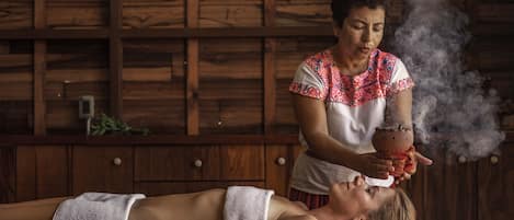 A person lying on a massage table in a wooden room with a towel over their body.