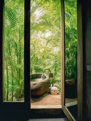 A window with a view of a natural setting, including a stone basin and bamboo plants.