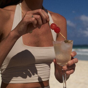A person holding a drink with a cherry on a stick.