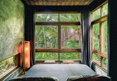 A room with a large window, a bed, a small table, and a lamp.