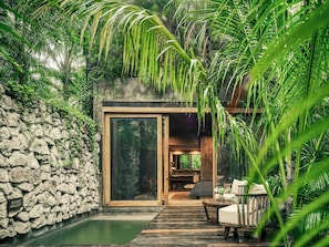 Un muro de piedra, una terraza de madera y una puerta de cristal que da a un espacio interior.