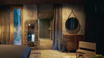 A room with a bed, a wooden dresser, a round mirror, and a stone wall.
