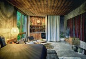 A room with a bed, a desk, a chair, a bookshelf, and a large window with greenery outside.