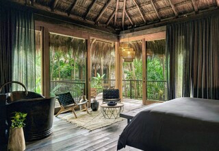 A room with a bed, a large window, a chair, a table, and a hanging light fixture.