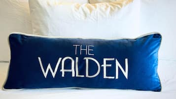 A bed with white bedding and a navy blue pillow with "THE WALDEN" embroidered on it.