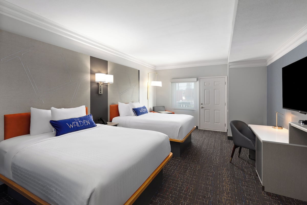 A hotel room with two beds, a desk, a television, and a door.