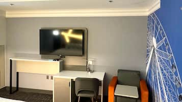 Quarto de hotel com cama, secretária com televisão, duas cadeiras e decoração na parede.