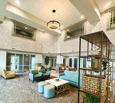 A spacious lobby with high ceilings, large windows, and a mix of seating areas including sofas and armchairs.