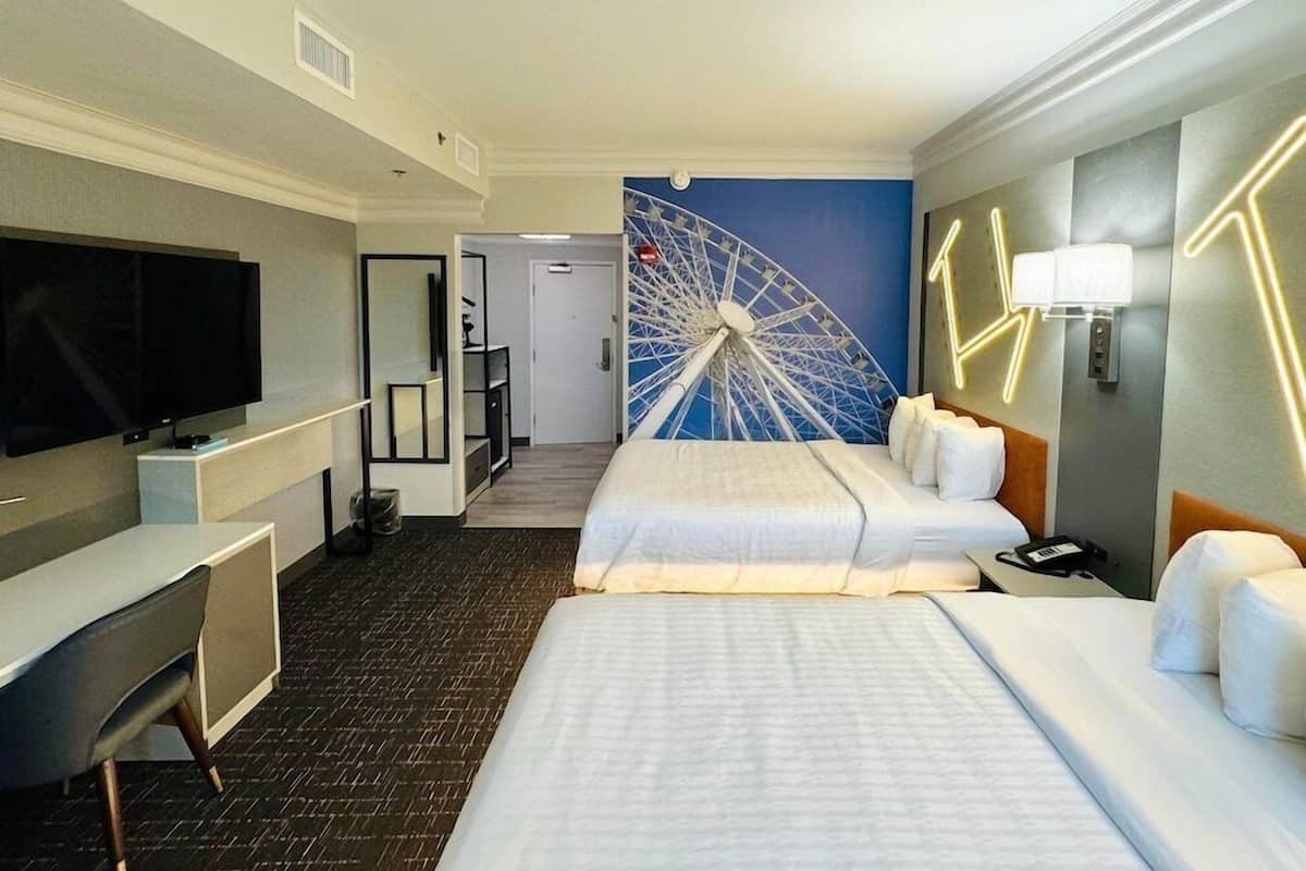 A hotel room with a bed, desk, TV, and a wall with a Ferris wheel mural.