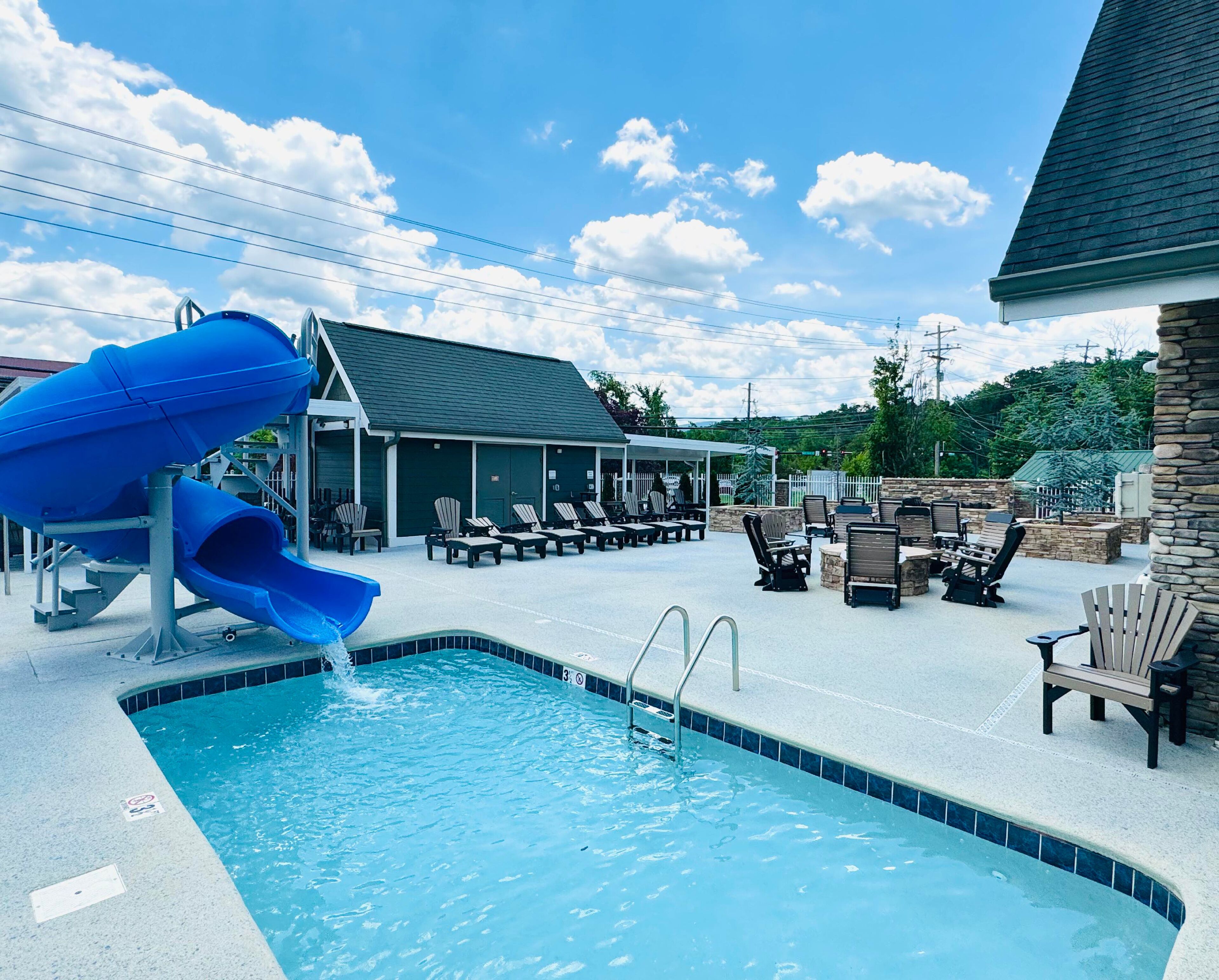 A swimming pool with a blue slide, lounge chairs, and a covered seating area.