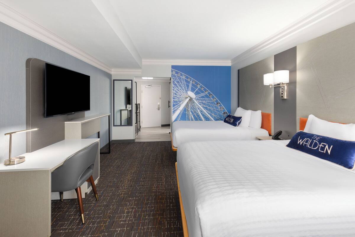 A hotel room with a large bed, a desk, a television, and a wall-mounted lamp.