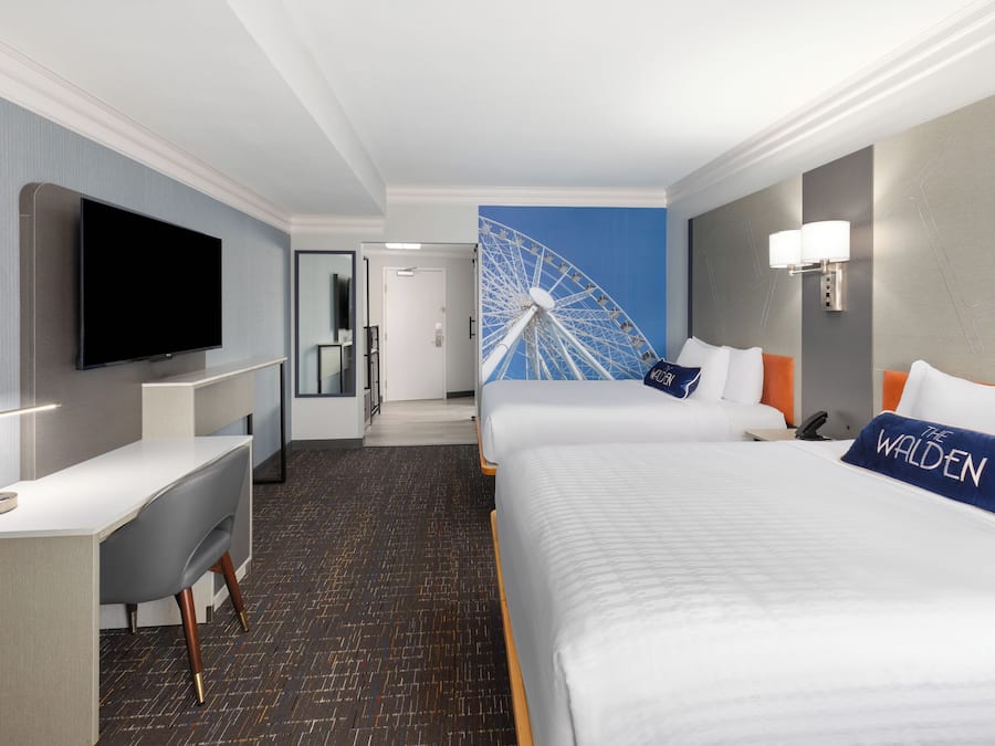 A hotel room with a large bed, a desk, a television, and a wall-mounted lamp.