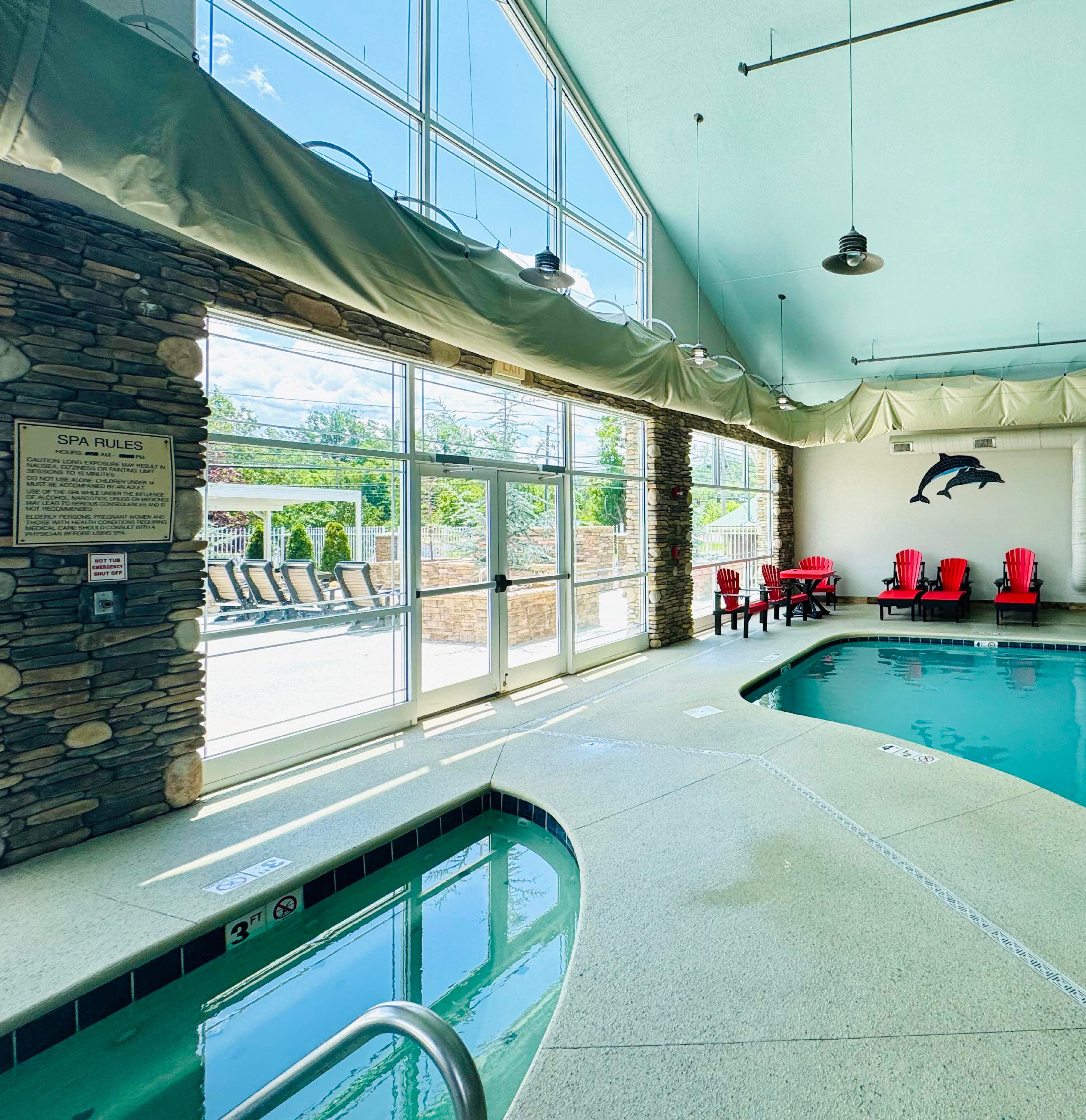 Una piscina interior con paredes de piedra, sillas rojas y un mural de delfines.
