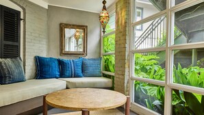 A cozy room with a sofa, a round table, and large windows with plants. - Hotel Saint Cecilia (Austin)