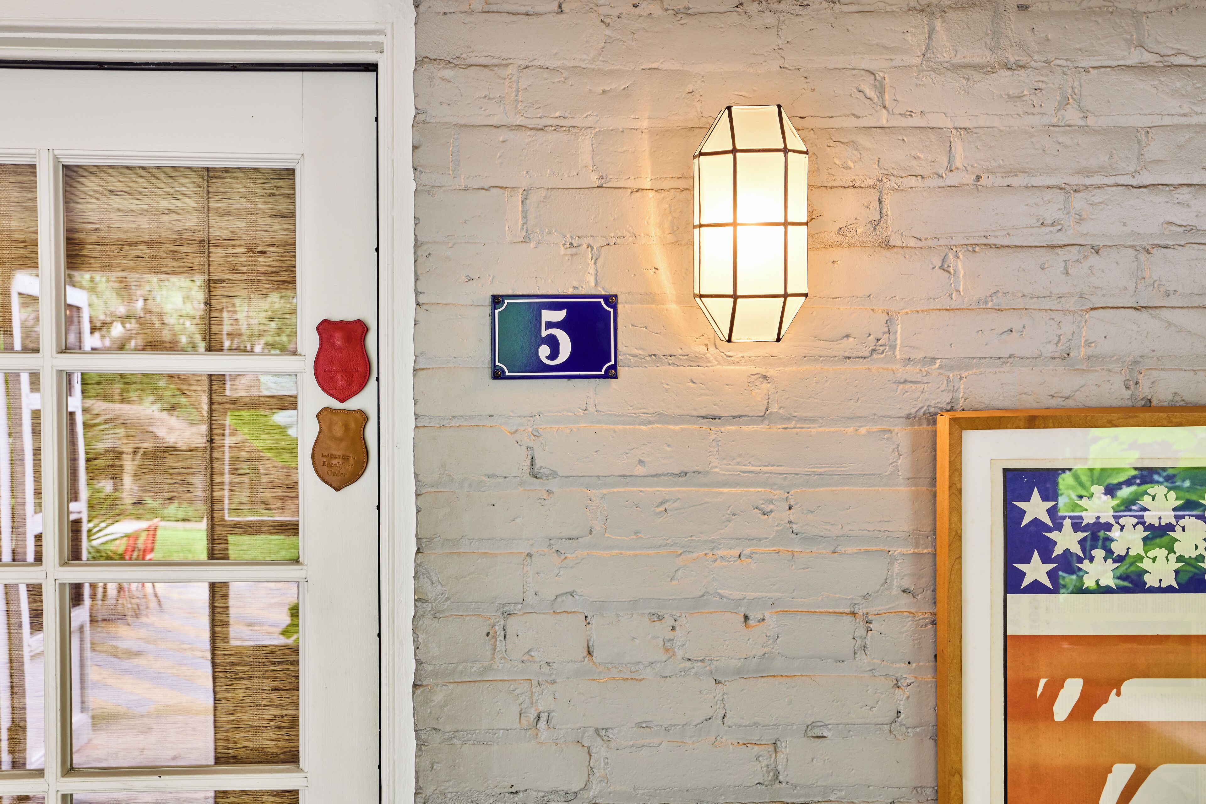 A brick wall with a lit wall lamp, a number plaque, and a shield-shaped decoration.