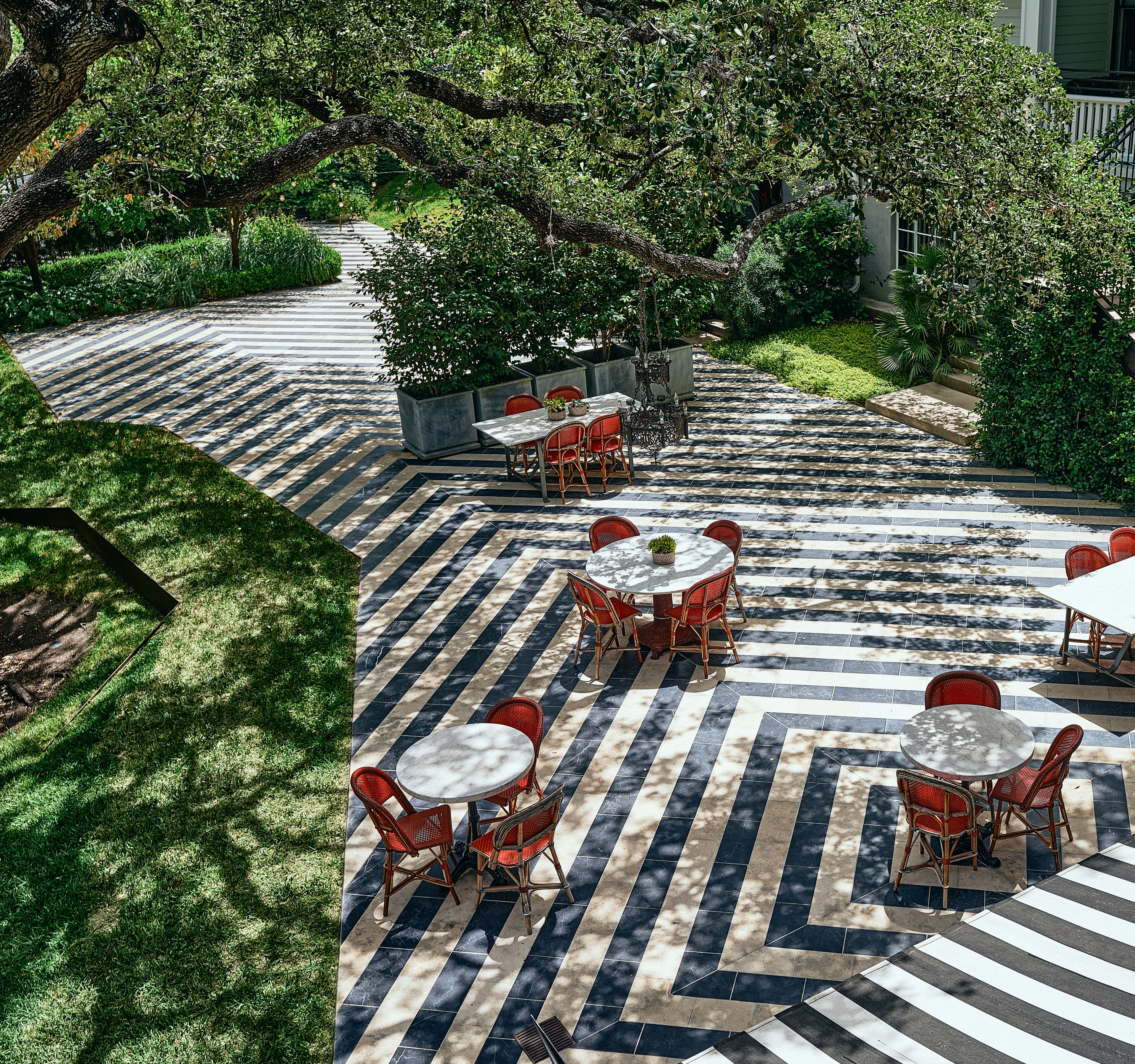 An outdoor patio with striped flooring, red wicker chairs, and round tables.