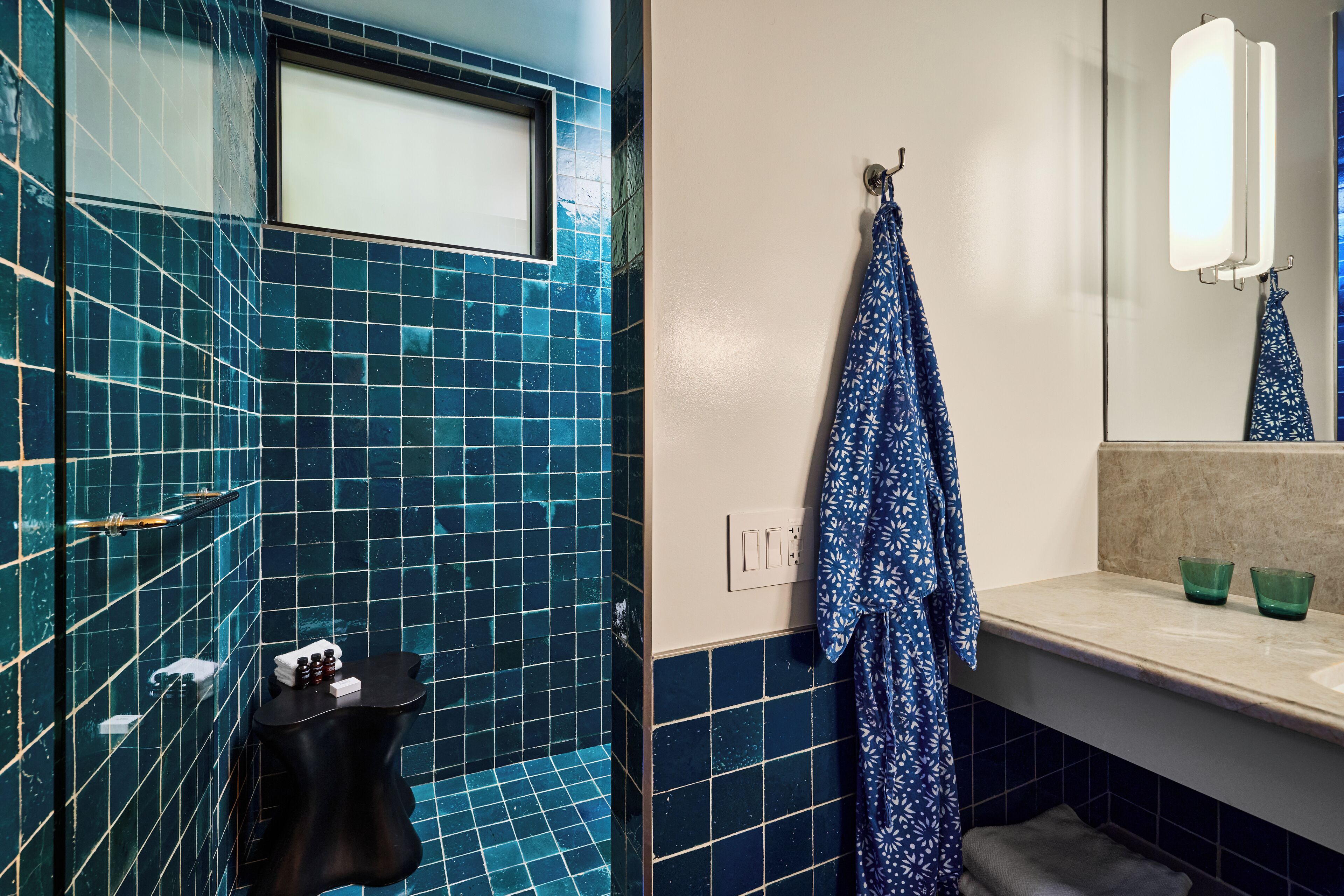 A bathroom with blue-tiled walls, a black vanity, a towel rack with a patterned towel, and a mirror with a light above it.