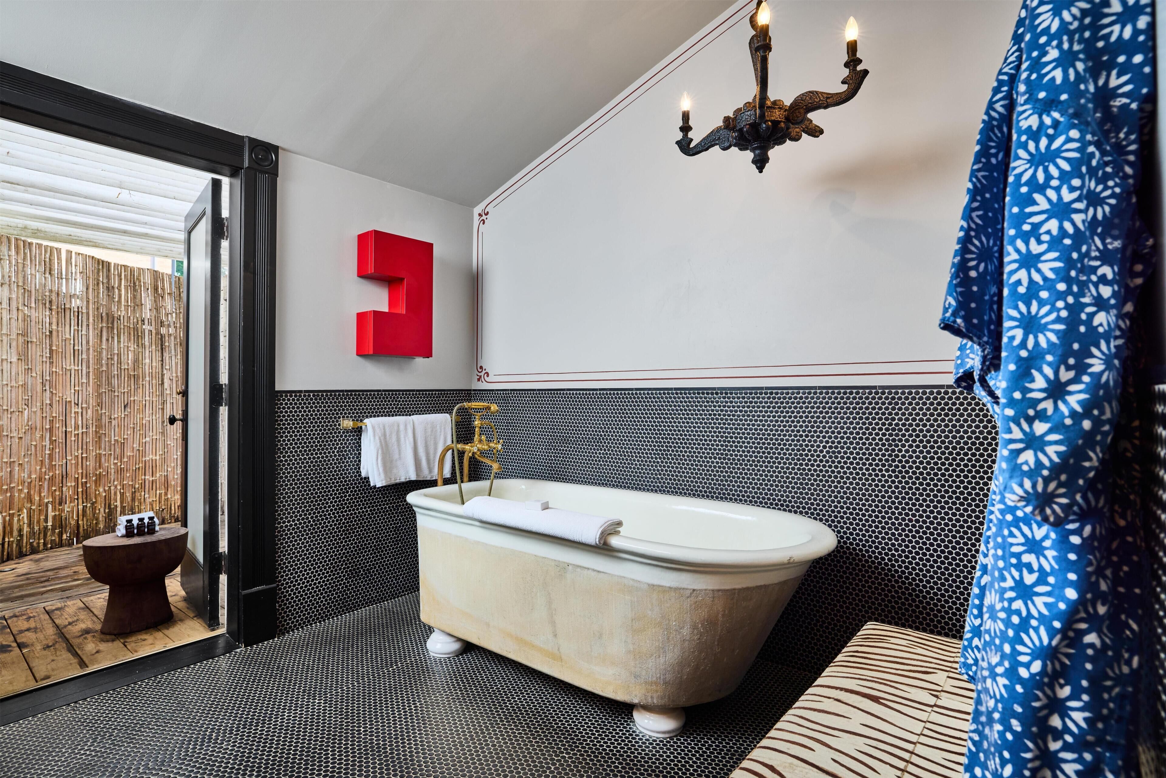 Ein modernes Badezimmer mit einer freistehenden Badewanne, einer roten Akzentwand, einem gemusterten Duschvorhang und einer Kristallleuchtreibe.