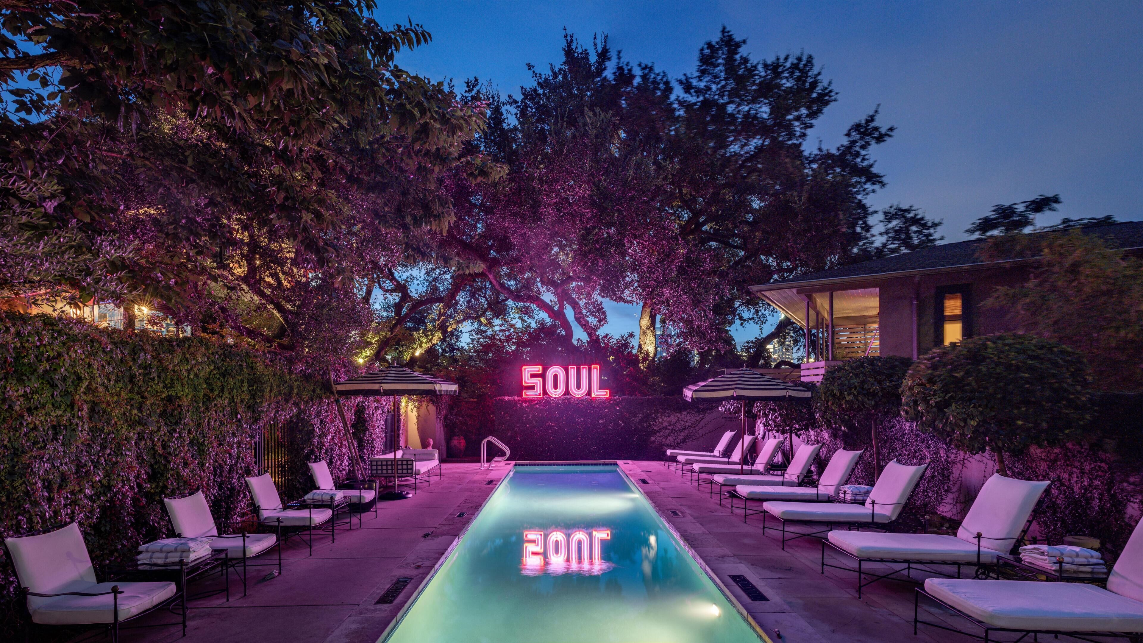 A pool area with lounge chairs, a neon sign reading 'SOUL,' and trees in the background.