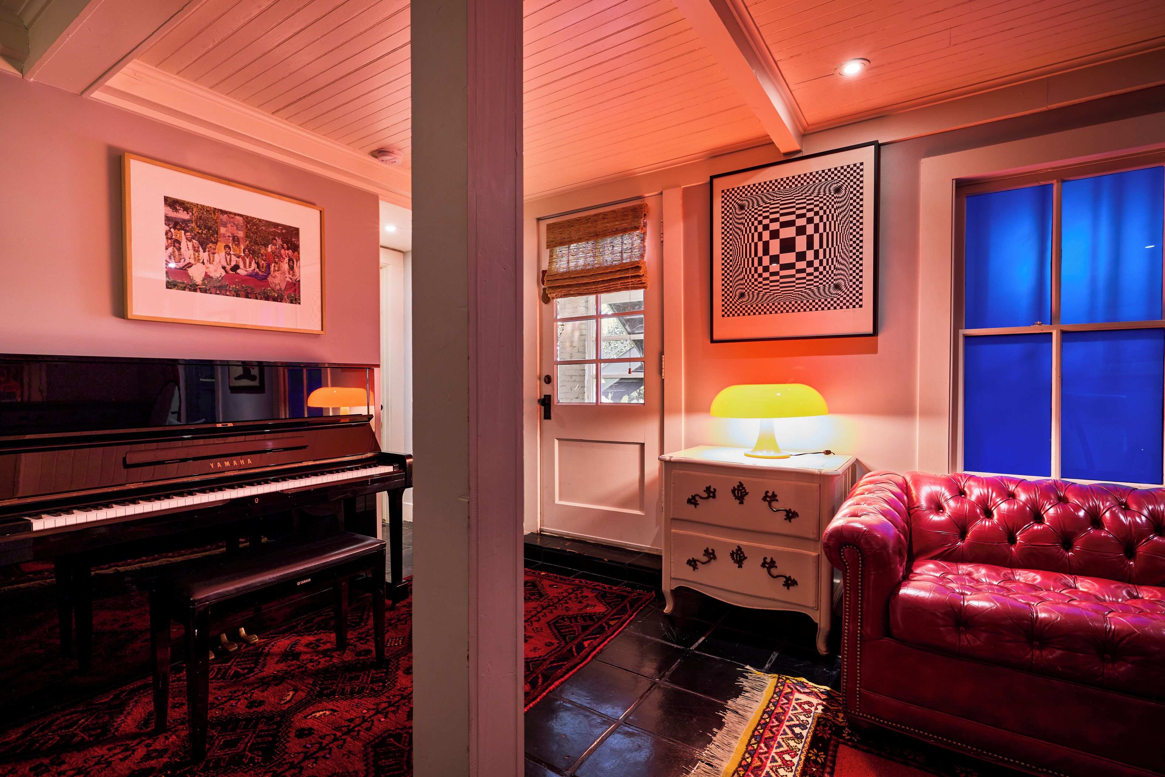 Une pièce avec un piano, un canapé en cuir rouge, un tapis à motifs et une œuvre d’art accrochée au mur.