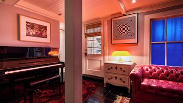 Une pièce avec un piano, un canapé en cuir rouge, un tapis à motifs et une œuvre d’art accrochée au mur.