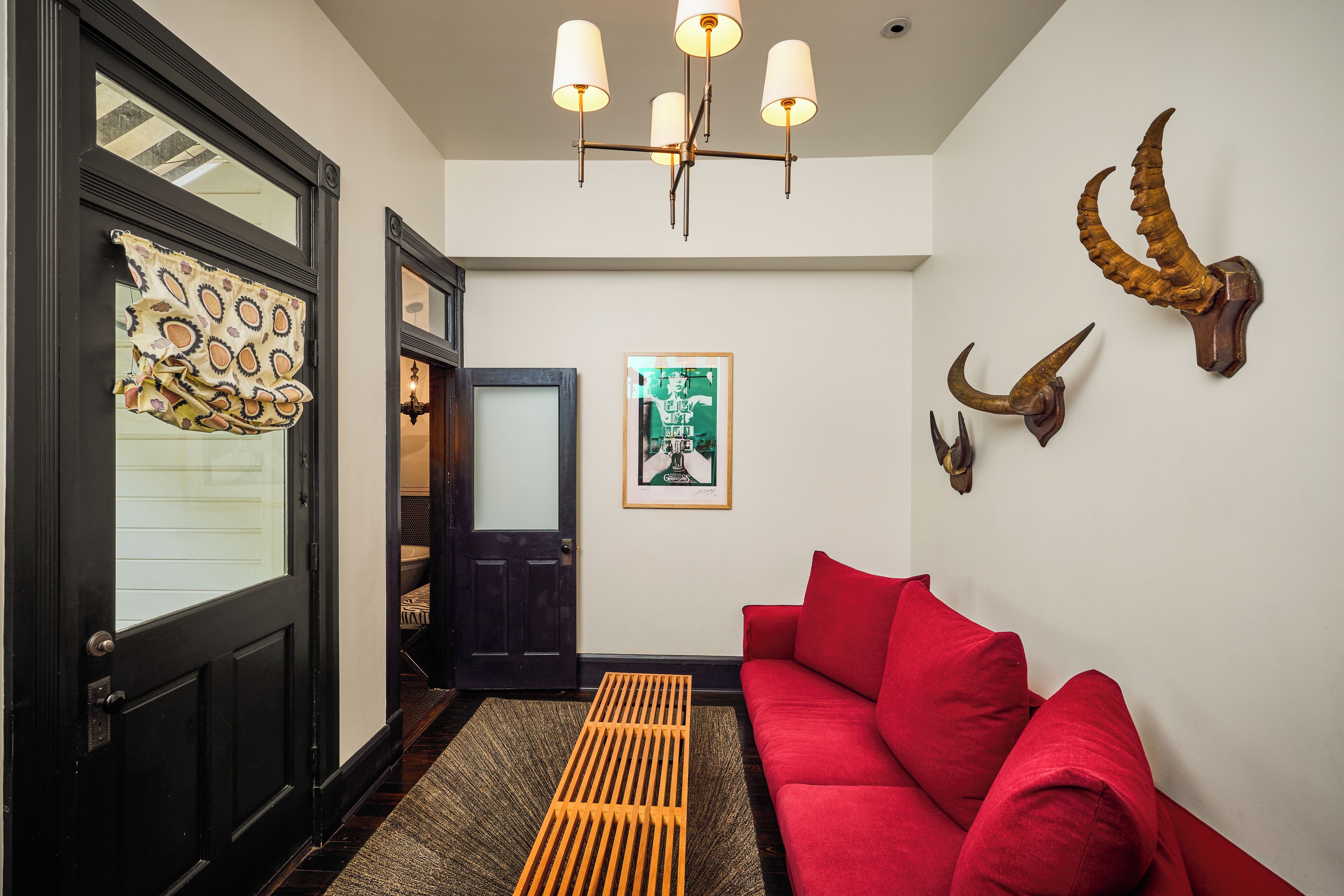 A modern interior with a red sofa, a wooden bench, a chandelier, and mounted animal horns on the wall.