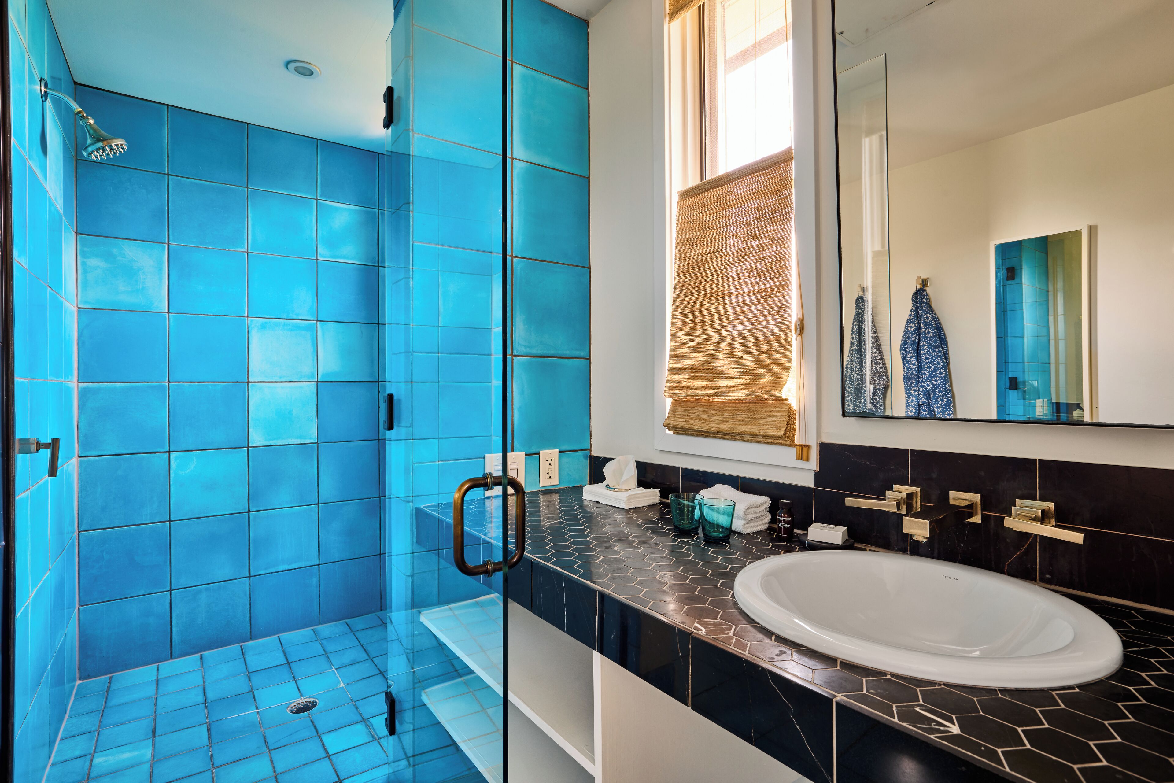 A bathroom with blue tiles, a glass shower enclosure, a white sink, and a large mirror.