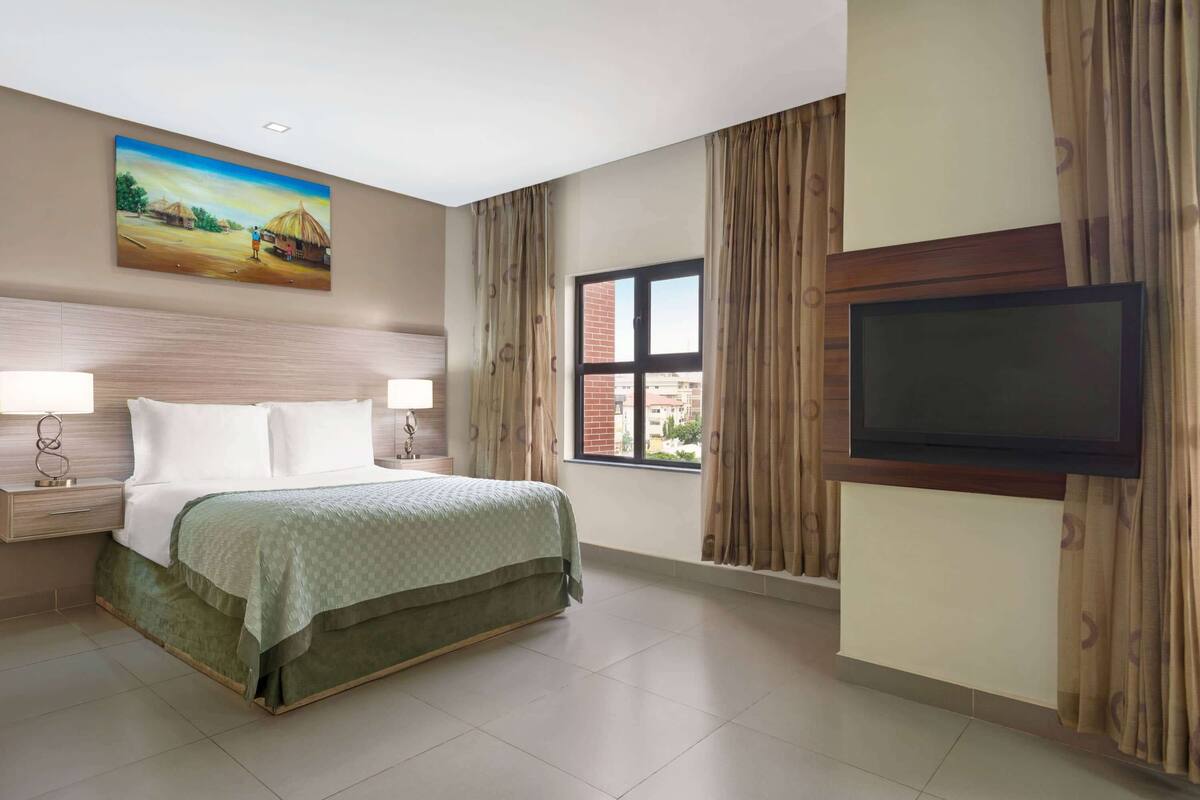 Une chambre d’hôtel avec un lit, des tables de chevet, une télévision et une grande fenêtre avec des rideaux.