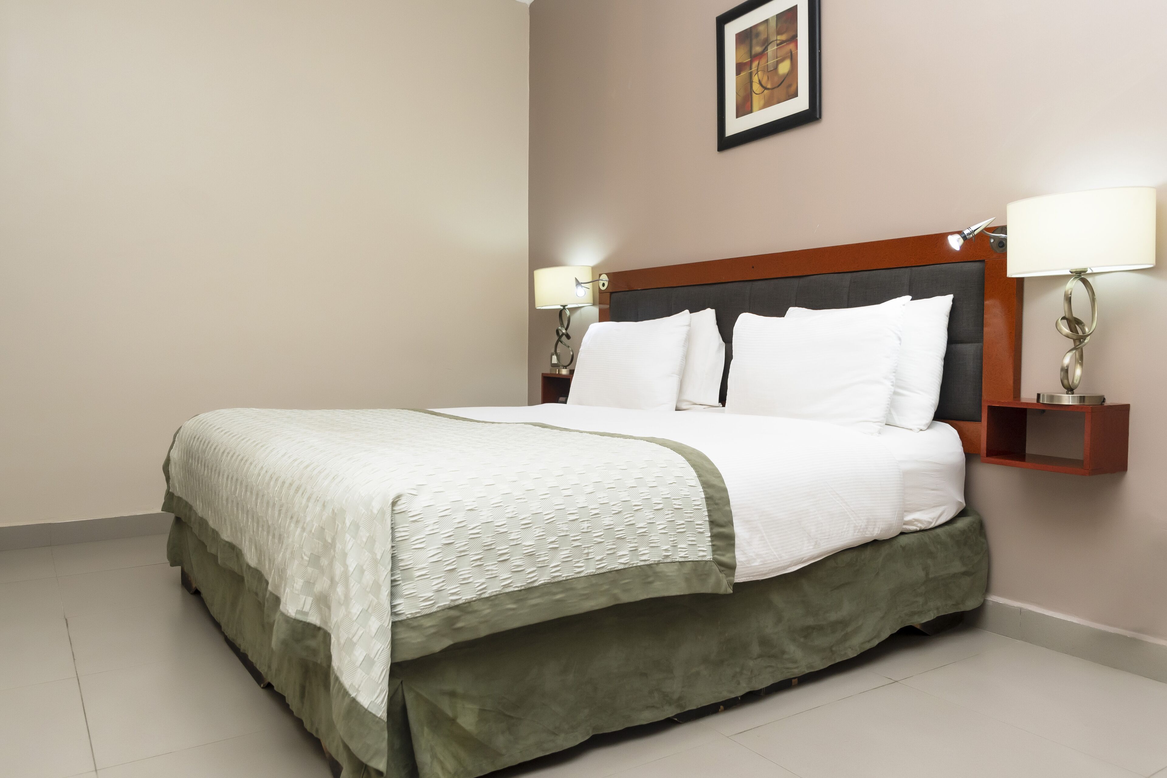 A neatly made bed with a green skirt, two bedside lamps, and a framed picture on the wall.