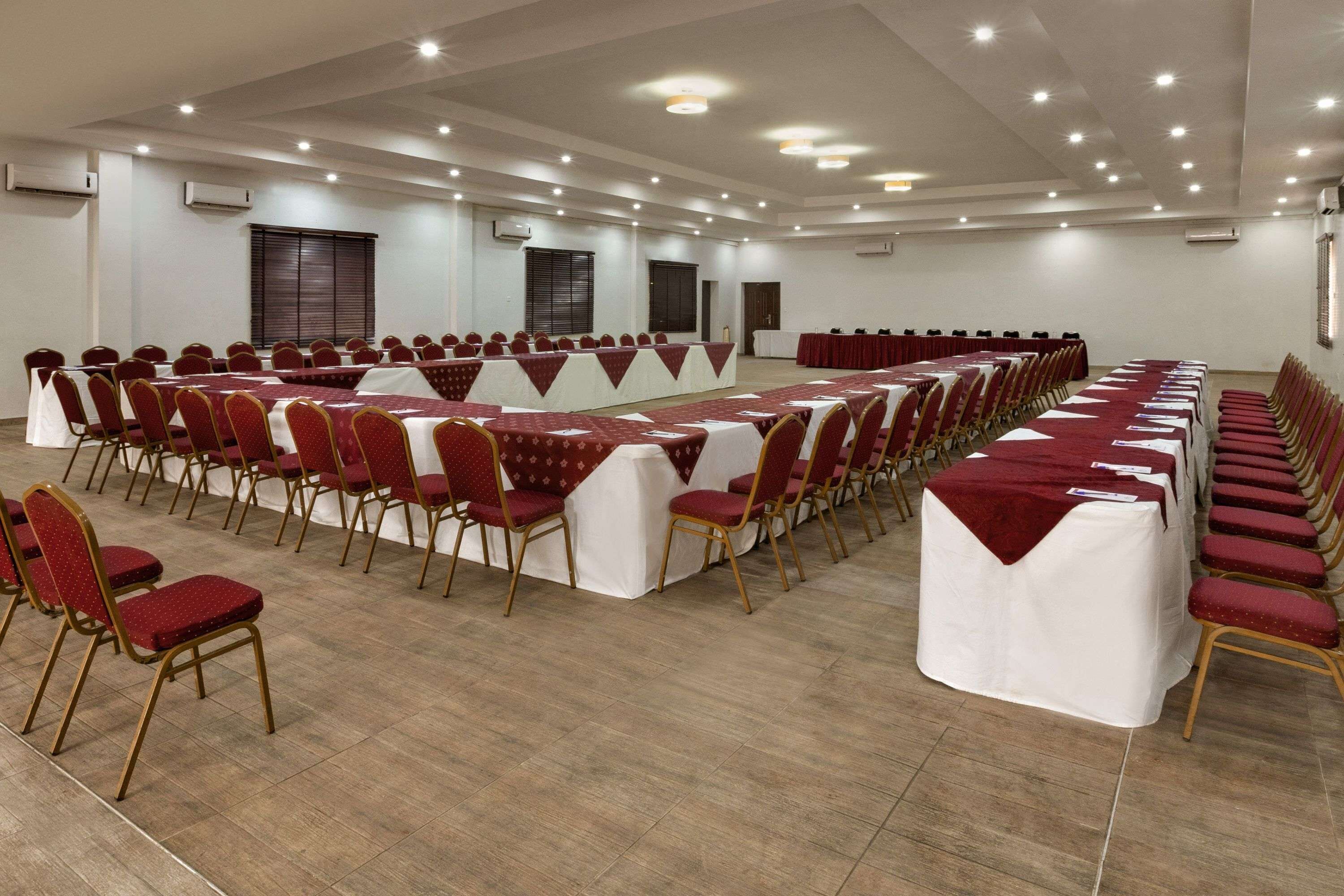 Une grande salle de conférence avec des rangées de tables et de chaises, des unités de climatisation et une porte.