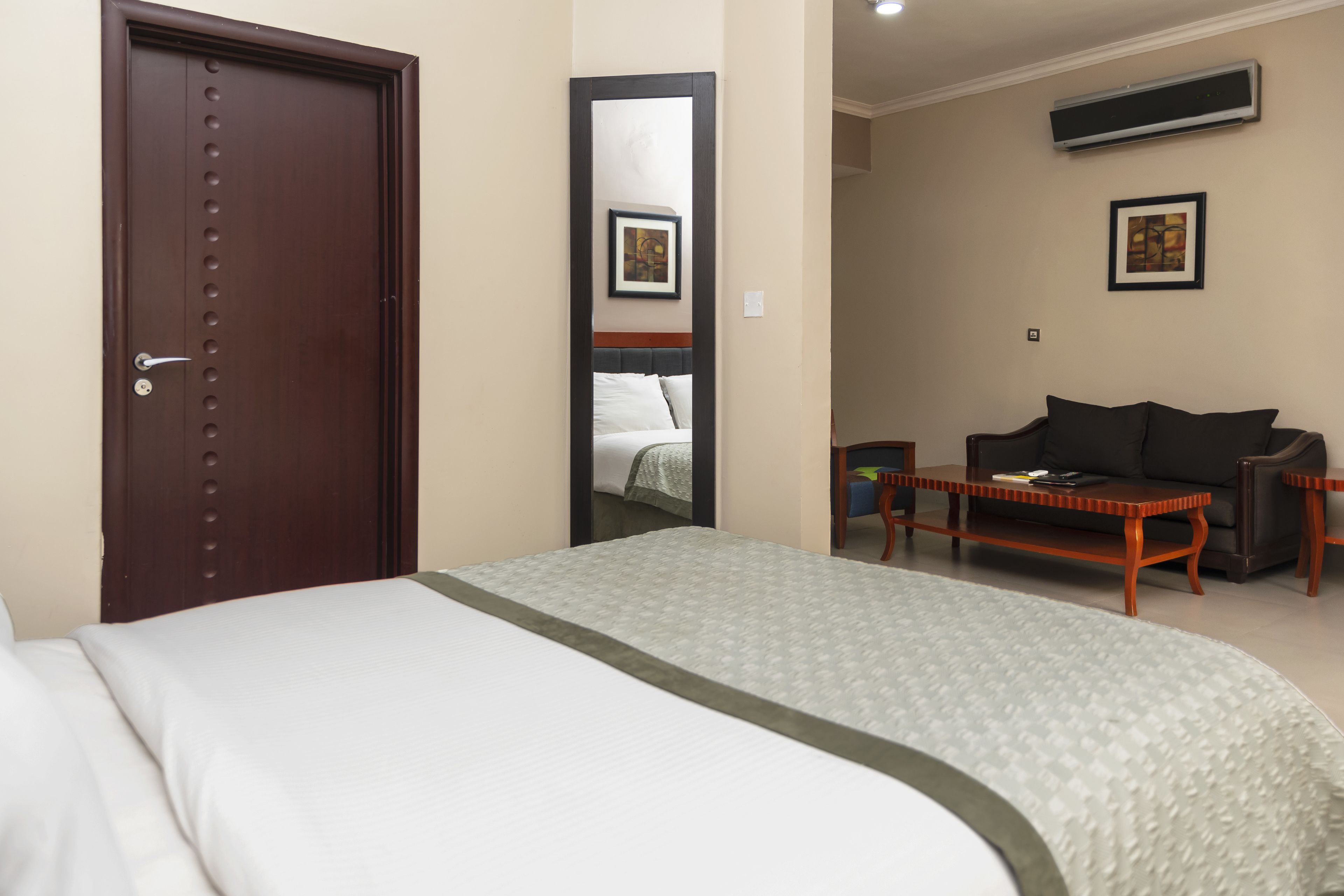 A hotel room with a large bed, a wooden nightstand, a sofa, and a mirror.