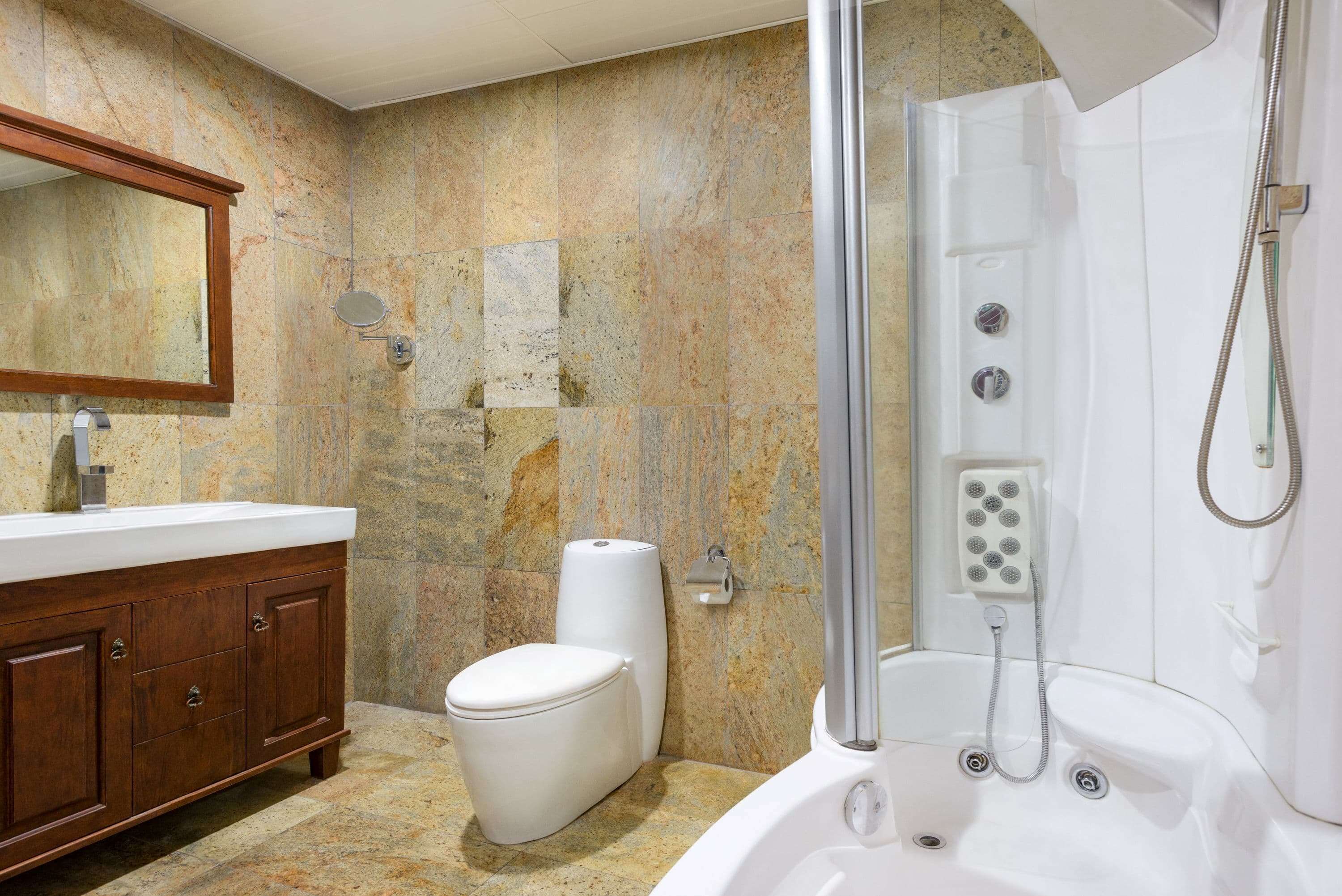 A bathroom with a marble wall, a wooden vanity, a toilet, and a bathtub with a showerhead.