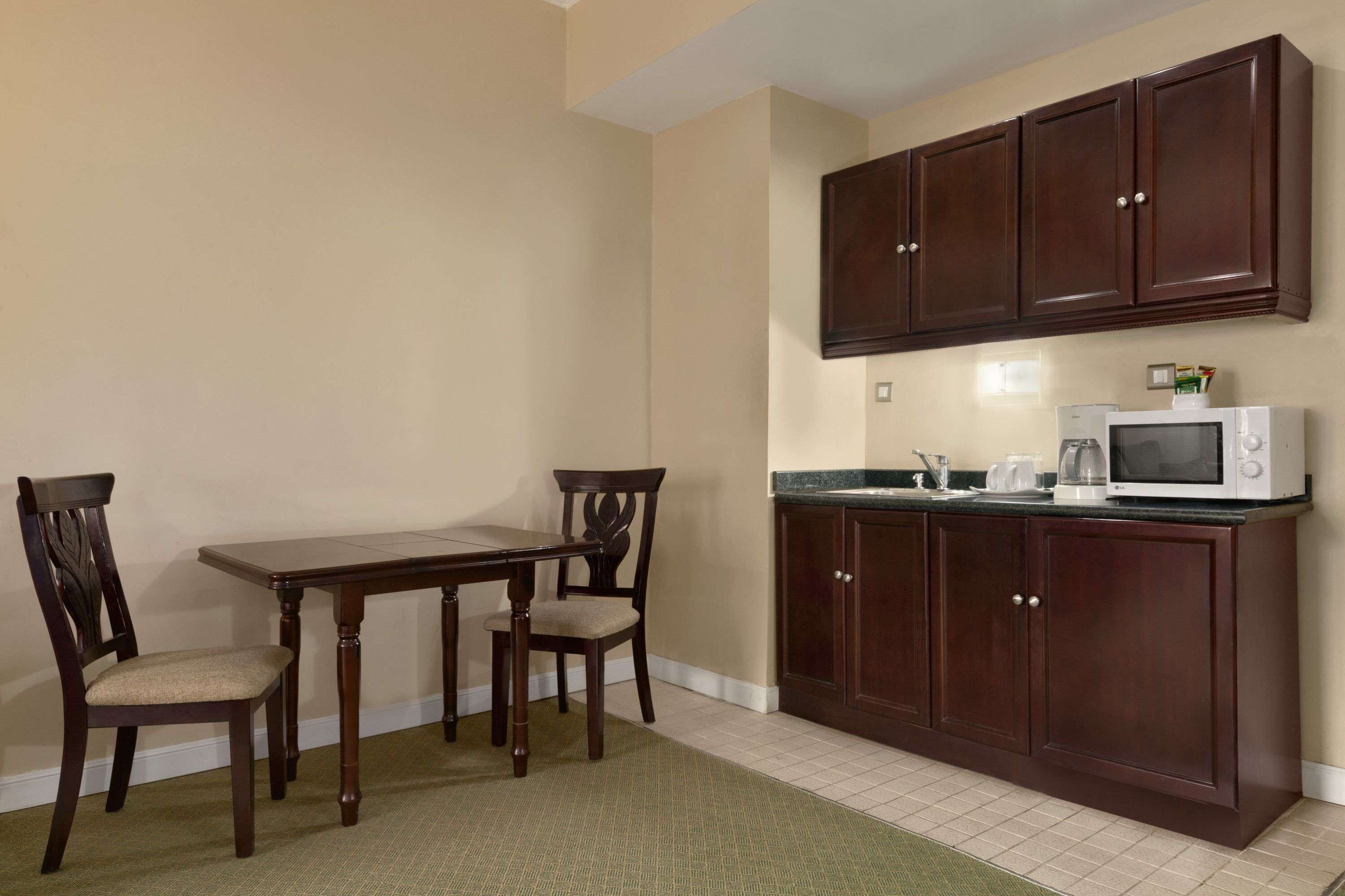 A kitchen with dark wooden cabinets, a white microwave, and a dining table with two chairs.