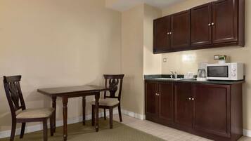 A kitchen with dark wooden cabinets, a white microwave, and a dining table with two chairs.