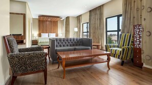 Een hotelkamer met een grijze bank, een fauteuil met dessin, een gestreepte fauteuil en een houten salontafel.