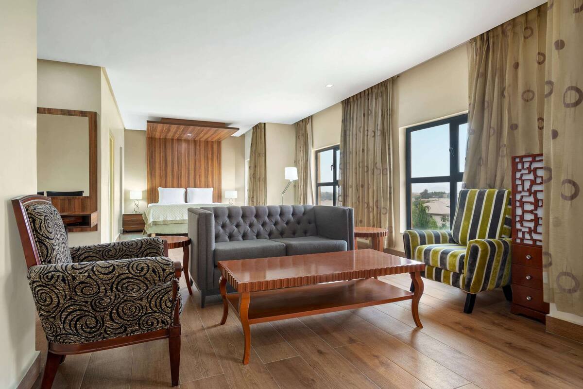 Une chambre d’hôtel avec un canapé gris, un fauteuil à motifs et un autre à rayures, ainsi qu’une table basse en bois.